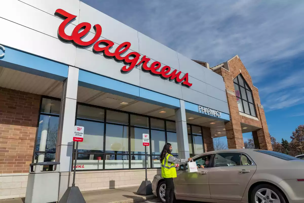 A person hands a bag to a customer in a car at the pickup area of a Walgreens store. A person hands a bag to a customer in a car at the pickup area of a Walgreens store.