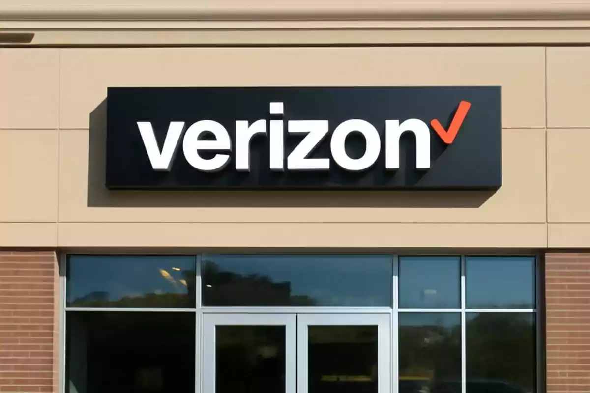Storefront with the Verizon logo on a black sign over a brick wall and beige panels. Storefront with the Verizon logo on a black sign over a brick wall and beige panels.