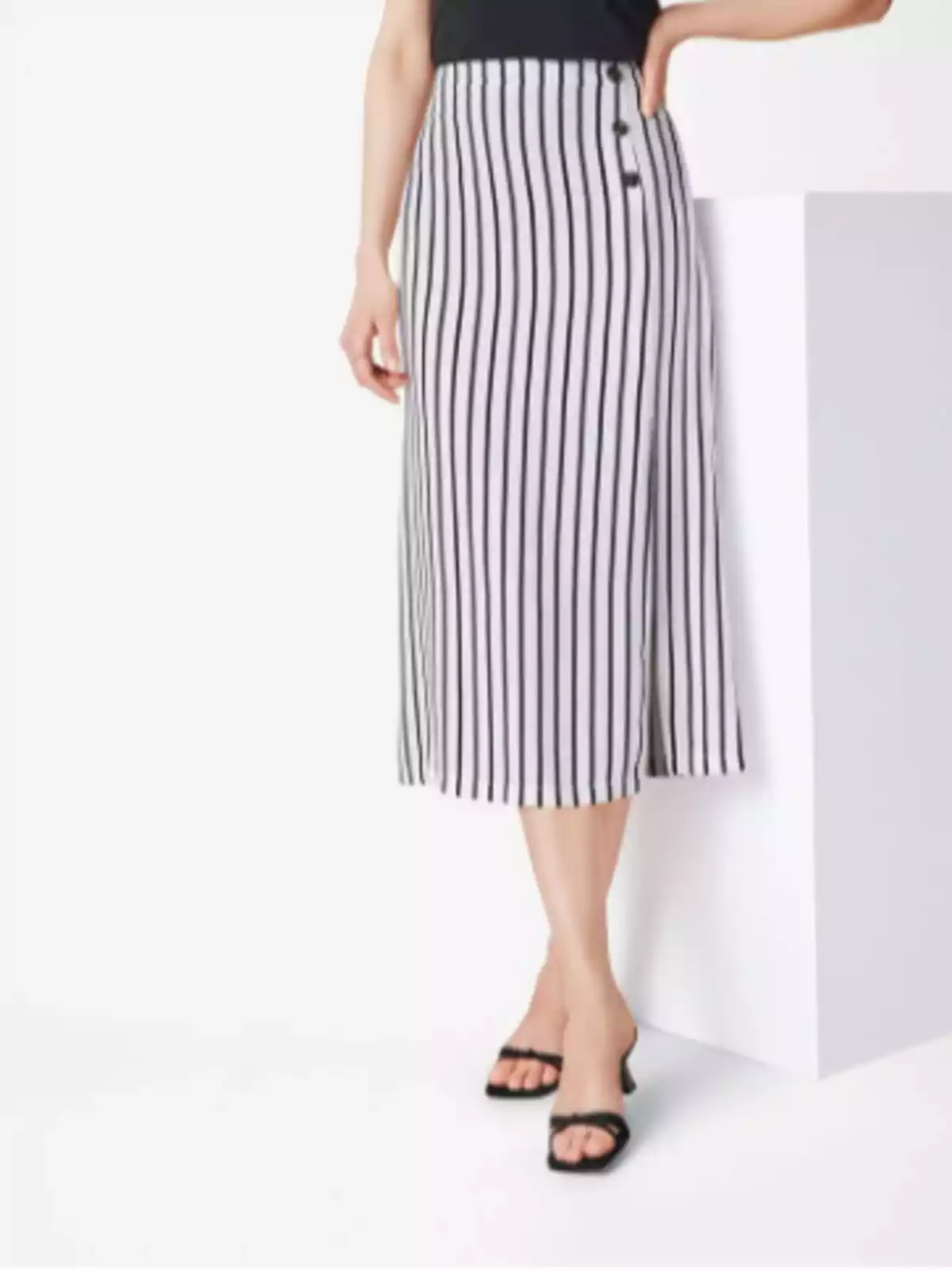 Mujer usando falda midi blanca con rayas verticales negras y sandalias de tacón negras Mujer usando falda midi blanca con rayas verticales negras y sandalias de tacón negras