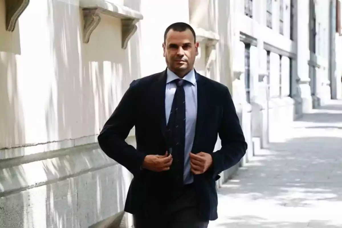A man in a dark suit walks down a street past a sunlit building. A man in a dark suit walks down a street past a sunlit building.