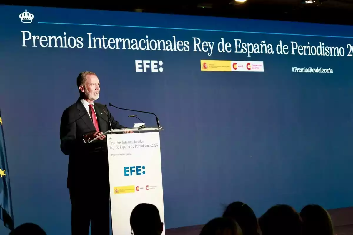 Felipe VI, wearing a dark suit, delivers a speech at a podium during the 2025 King of Spain International Journalism Awards ceremony, with a blue background displaying the event name and institutional logos.