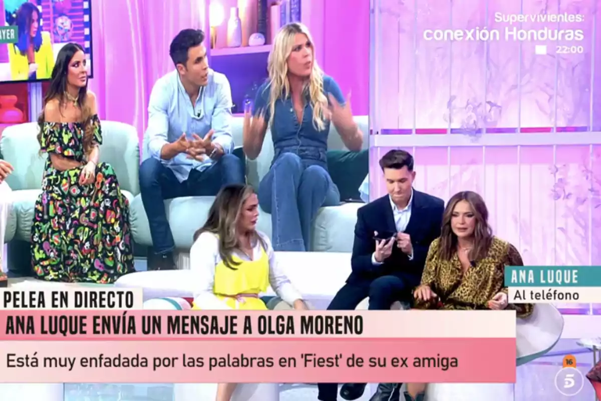 Un grupo de personas está sentado en un set de televisión con una decoración en tonos rosados y morados, mientras discuten un tema que aparece en un rótulo en la parte inferior de la imagen. Un grupo de personas está sentado en un set de televisión con una decoración en tonos rosados y morados, mientras discuten un tema que aparece en un rótulo en la parte inferior de la imagen.