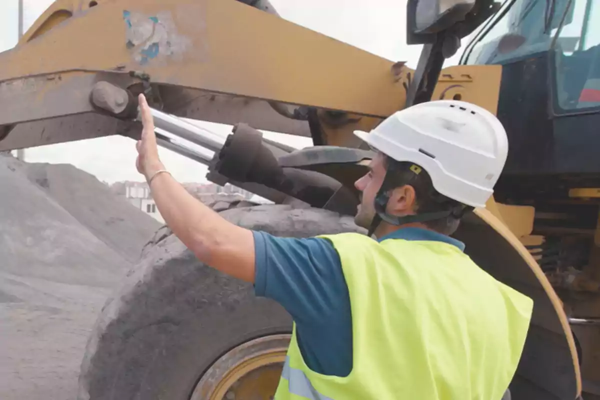 Trabajador de la construcción con casco y chaleco de seguridad dirigiendo una máquina pesada en un sitio de construcción.