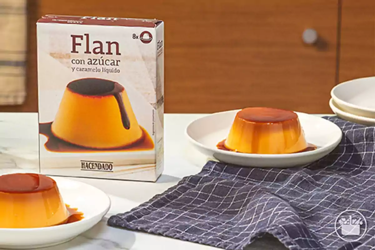 Caja de flan con azúcar y caramelo líquido de la marca Hacendado junto a dos porciones servidas en platos sobre un mantel azul. Caja de flan con azúcar y caramelo líquido de la marca Hacendado junto a dos porciones servidas en platos sobre un mantel azul.