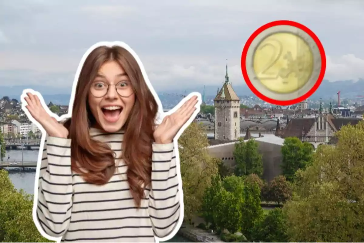 Una mujer sonriente con gafas y suéter a rayas levanta las manos en un gesto de sorpresa frente a un paisaje urbano con una torre y un gran árbol, mientras una moneda de dos euros está resaltada en un círculo rojo en la esquina superior derecha.