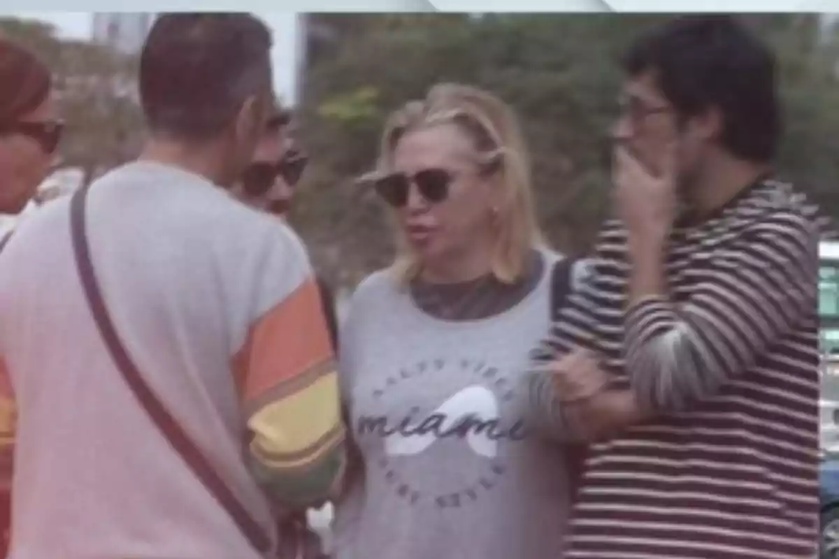 Un grupo de personas conversando al aire libre, una de ellas lleva una camiseta con la palabra 