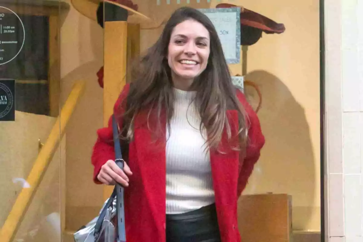 Eva Fernández con cabello largo y suelto, sonriente, usando un abrigo rojo y un suéter blanco, saliendo de una tienda Eva Fernández con cabello largo y suelto, sonriente, usando un abrigo rojo y un suéter blanco, saliendo de una tienda