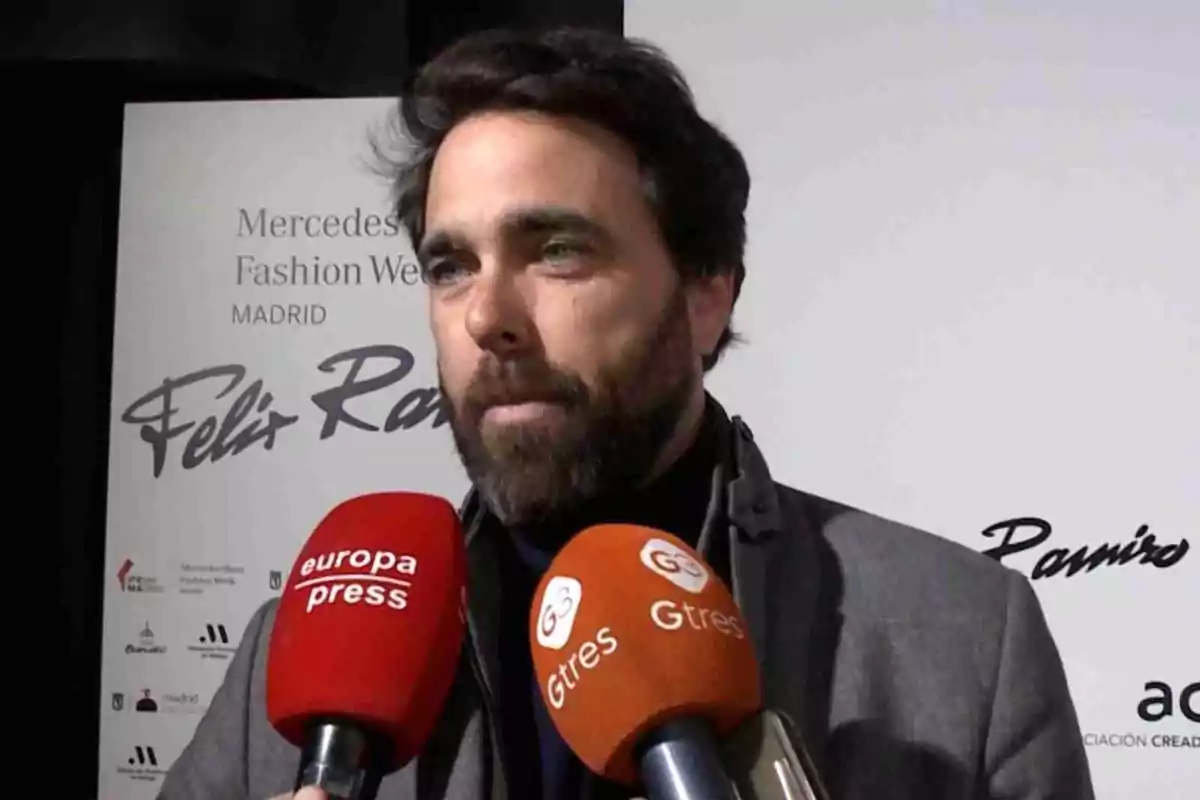 Javier Ungría con barba y cabello oscuro está hablando frente a varios micrófonos de prensa en un evento de moda en Madrid. Javier Ungría con barba y cabello oscuro está hablando frente a varios micrófonos de prensa en un evento de moda en Madrid.