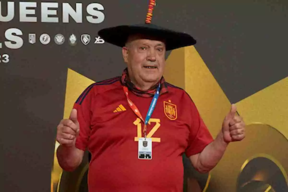 Manolo El del Bombo con camiseta roja de España y sombrero negro sonríe y levanta los pulgares frente a un fondo decorativo. Manolo El del Bombo con camiseta roja de España y sombrero negro sonríe y levanta los pulgares frente a un fondo decorativo.
