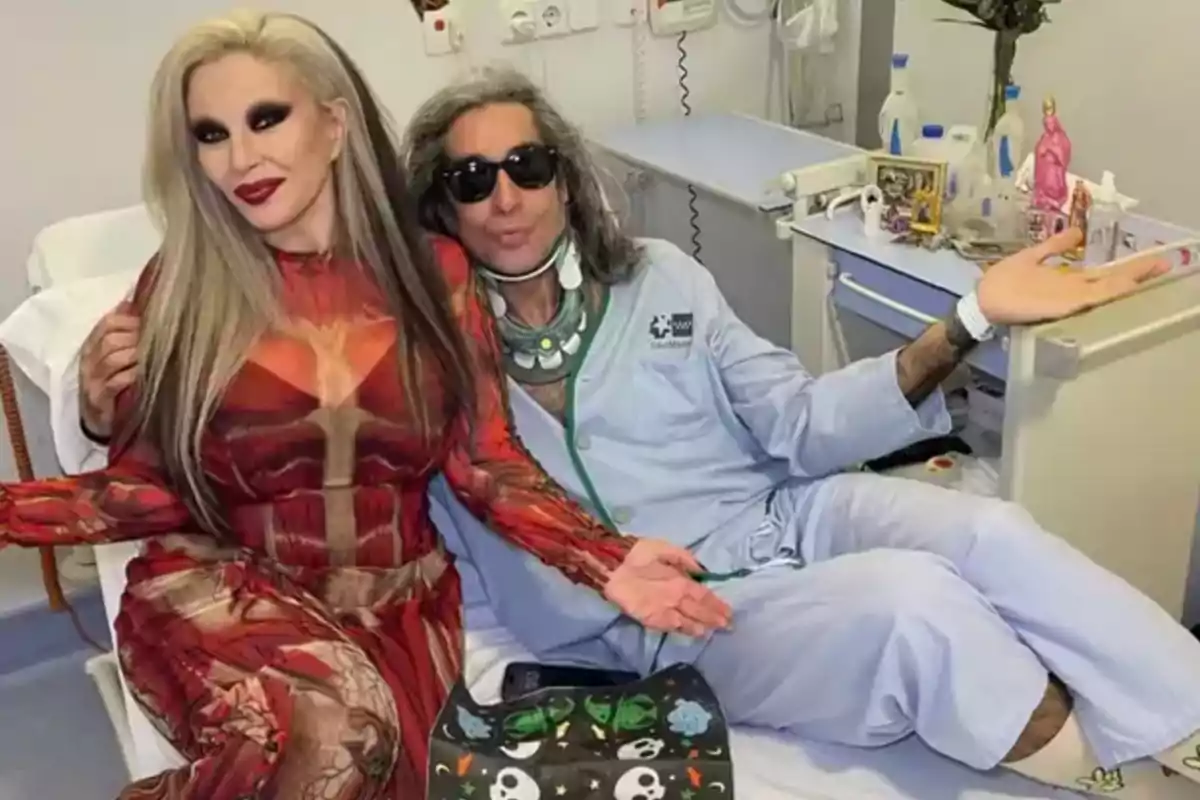 Una persona con un vestido rojo y otra con pijama de hospital posan juntas en una habitación médica. Una persona con un vestido rojo y otra con pijama de hospital posan juntas en una habitación médica.