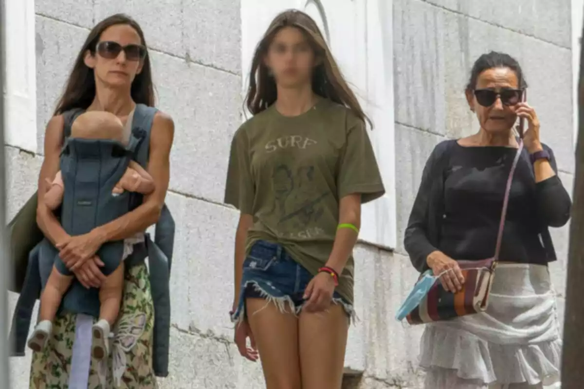 Telma Ortiz, her daughter Amanda and Paloma Rocasolano walking down the street, one of them is carrying a baby in a baby carrier, another is wearing a green t-shirt and jean shorts, and the third is talking on a mobile phone. Telma Ortiz, her daughter Amanda and Paloma Rocasolano walking down the street, one of them is carrying a baby in a baby carrier, another is wearing a green t-shirt and jean shorts, and the third is talking on a mobile phone.