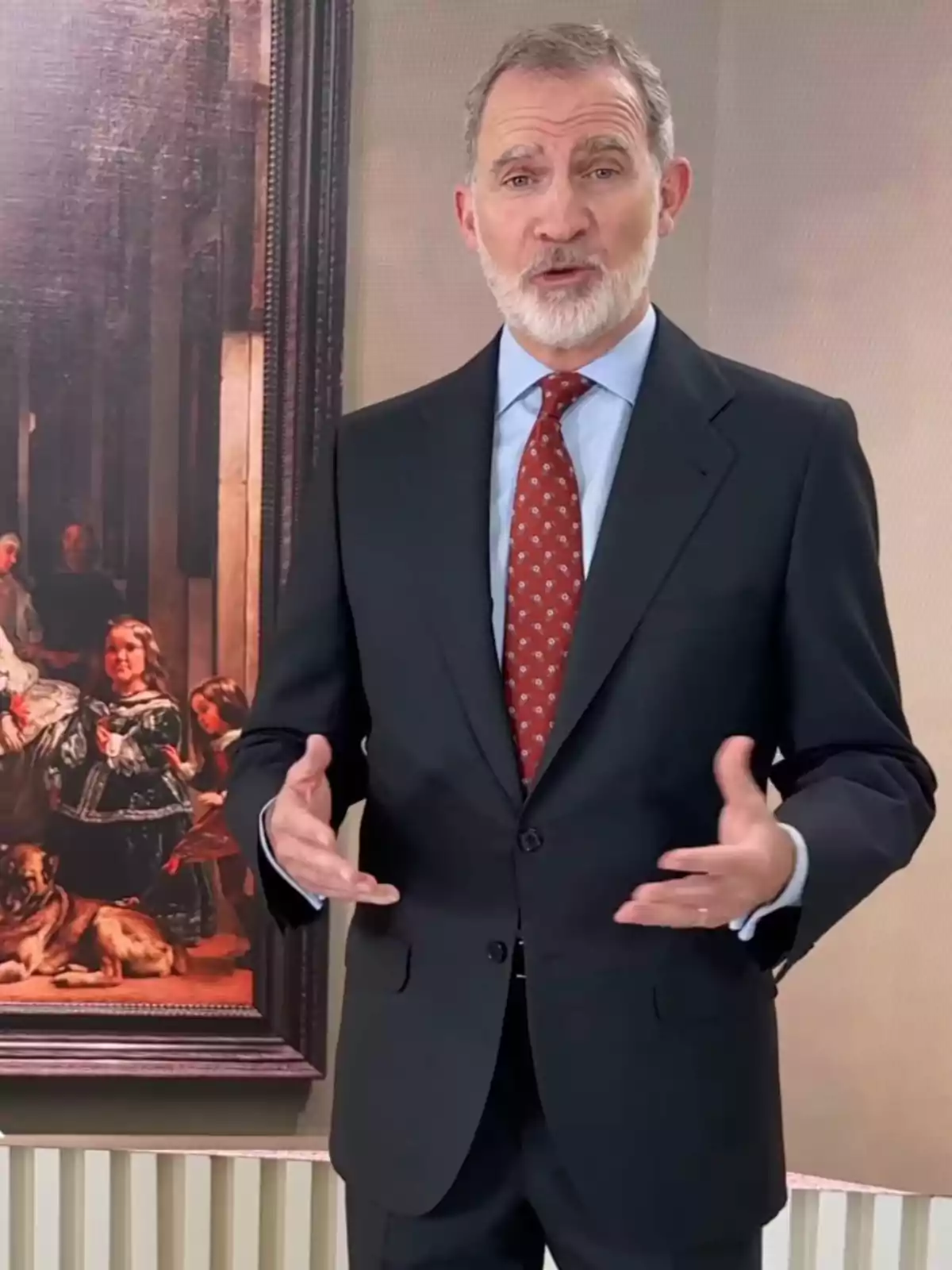 El rey Felipe VI de cabello canoso y barba vestido con traje oscuro y corbata roja posando frente a 'Las meninas' de Veláquez El rey Felipe VI de cabello canoso y barba vestido con traje oscuro y corbata roja posando frente a 'Las meninas' de Veláquez
