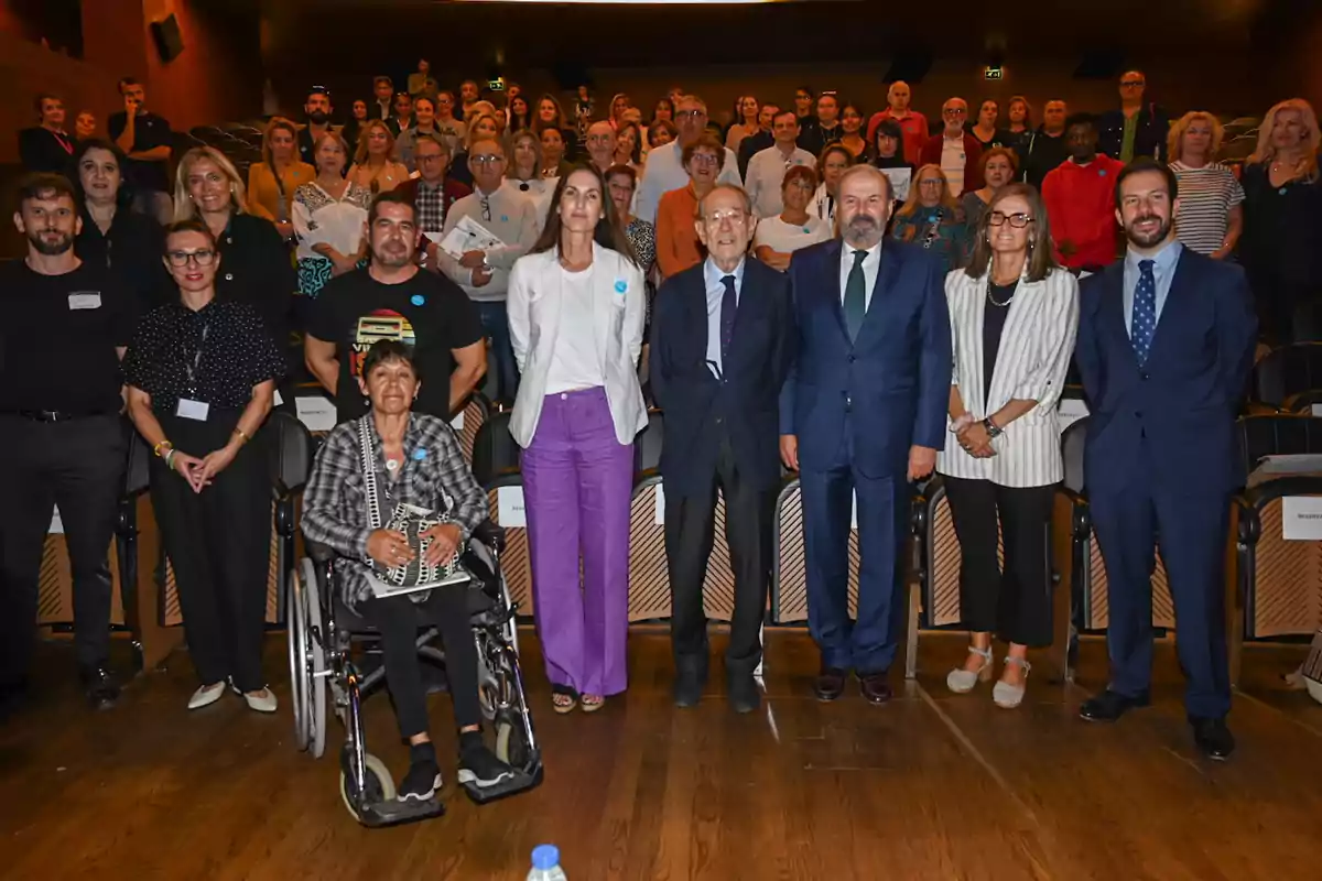 Un grupo de personas posando para una foto en un auditorio, con algunas personas en la primera fila y otras de pie en las filas traseras.