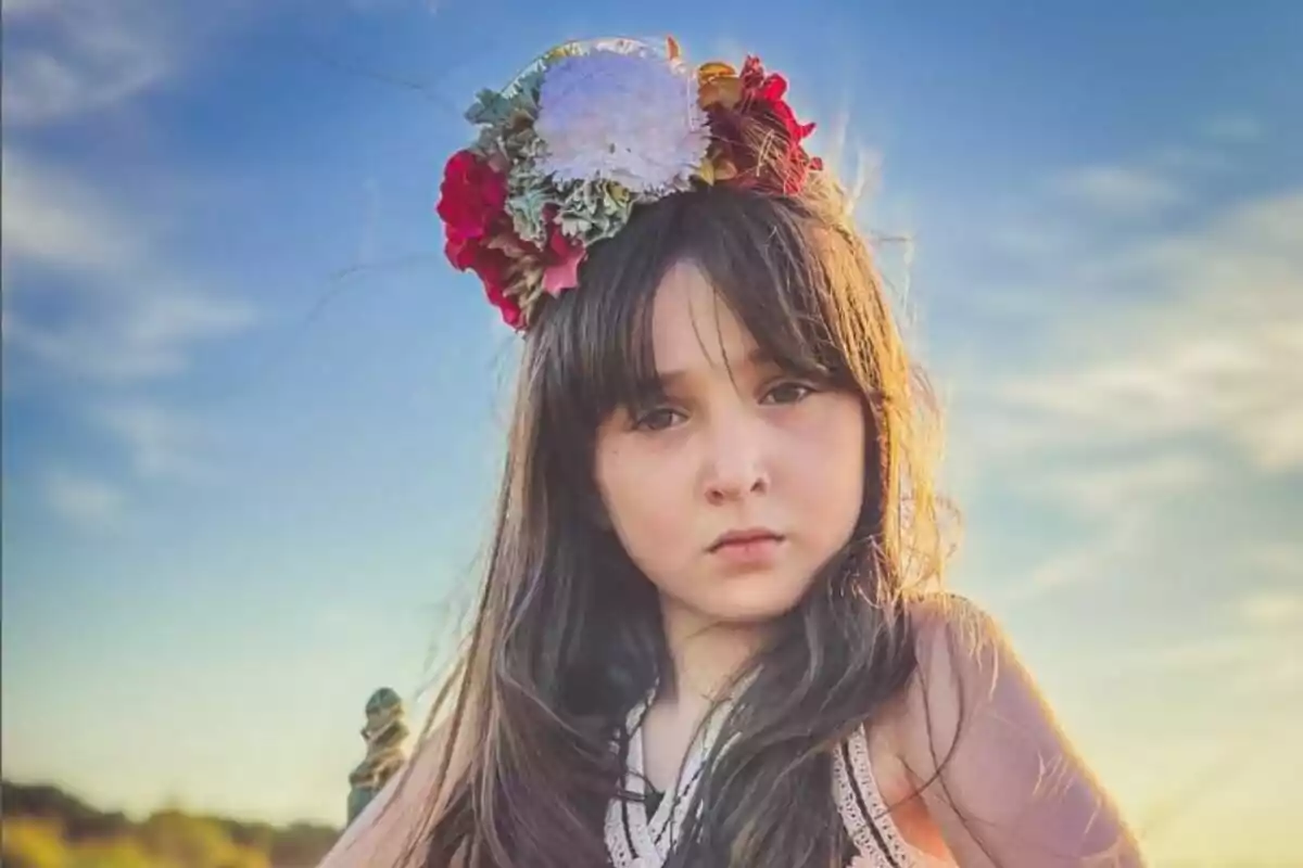 Niña con corona de flores en un campo al atardecer.