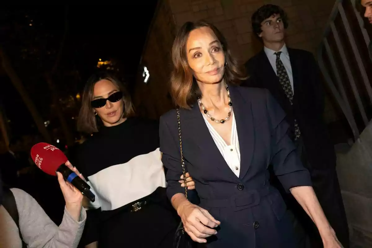 Tamara Falcó y Isabel Preysler caminando, una de ellas con gafas de sol y la otra con un collar de perlas, mientras una persona sostiene un micrófono rojo de Tamara Falcó y Isabel Preysler caminando, una de ellas con gafas de sol y la otra con un collar de perlas, mientras una persona sostiene un micrófono rojo de