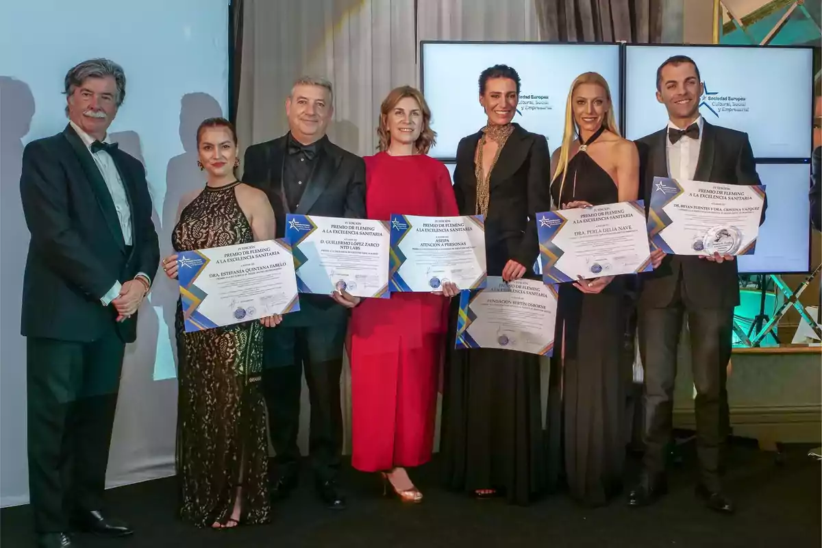 Un grupo de personas vestidas de gala posando con certificados en un evento de premiación.