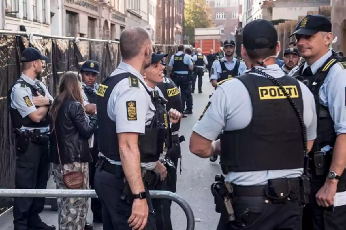 Un grupo de policías se encuentra en una calle, algunos conversando entre ellos y otros vigilando el área.