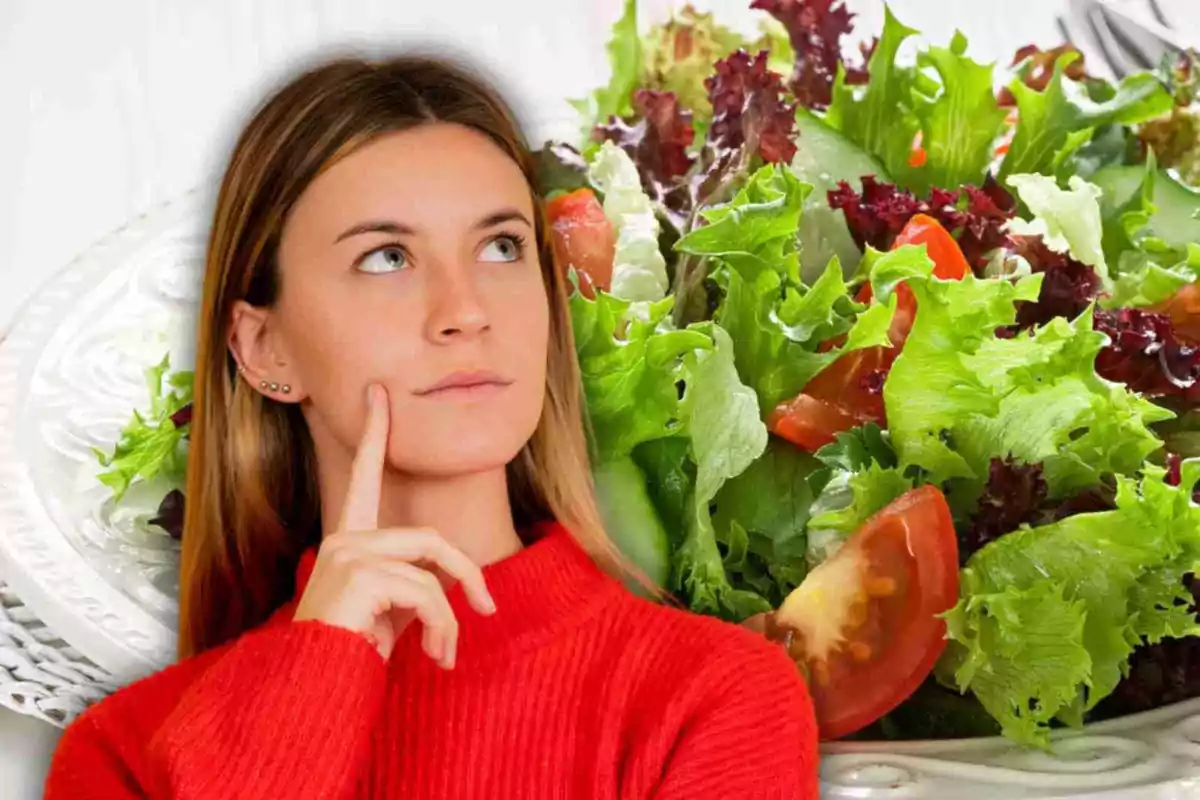 Mujer pensativa con un suéter rojo frente a un plato de ensalada.