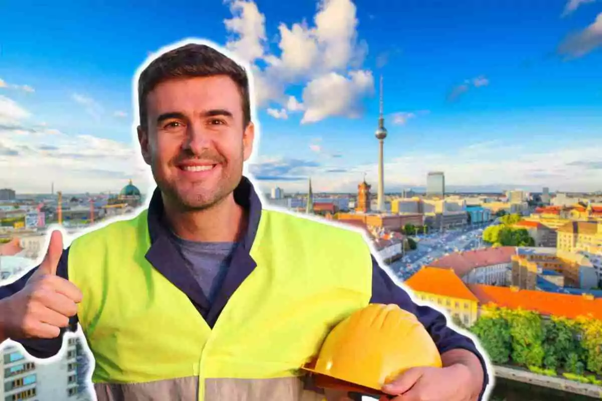 Hombre con chaleco de seguridad y casco amarillo en mano, sonriendo y mostrando el pulgar hacia arriba con una ciudad de fondo.