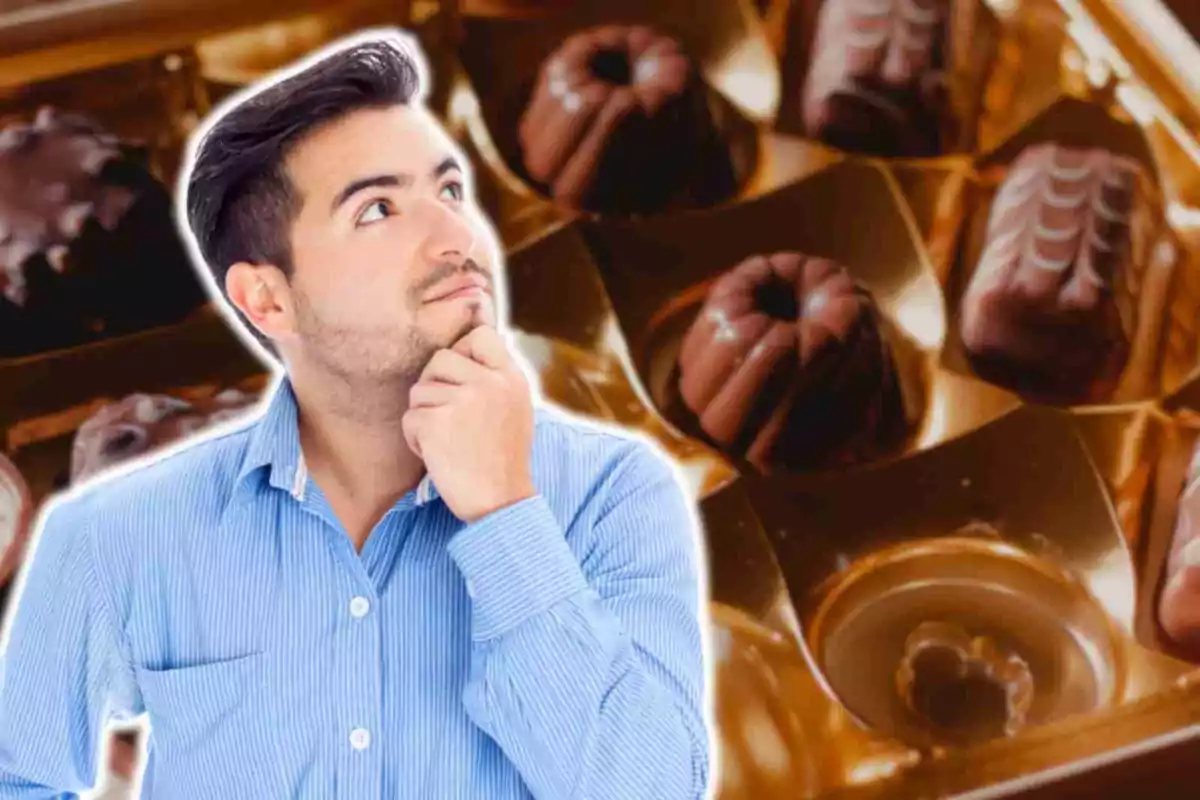 Hombre pensativo con camisa azul frente a una caja de bombones de chocolate.