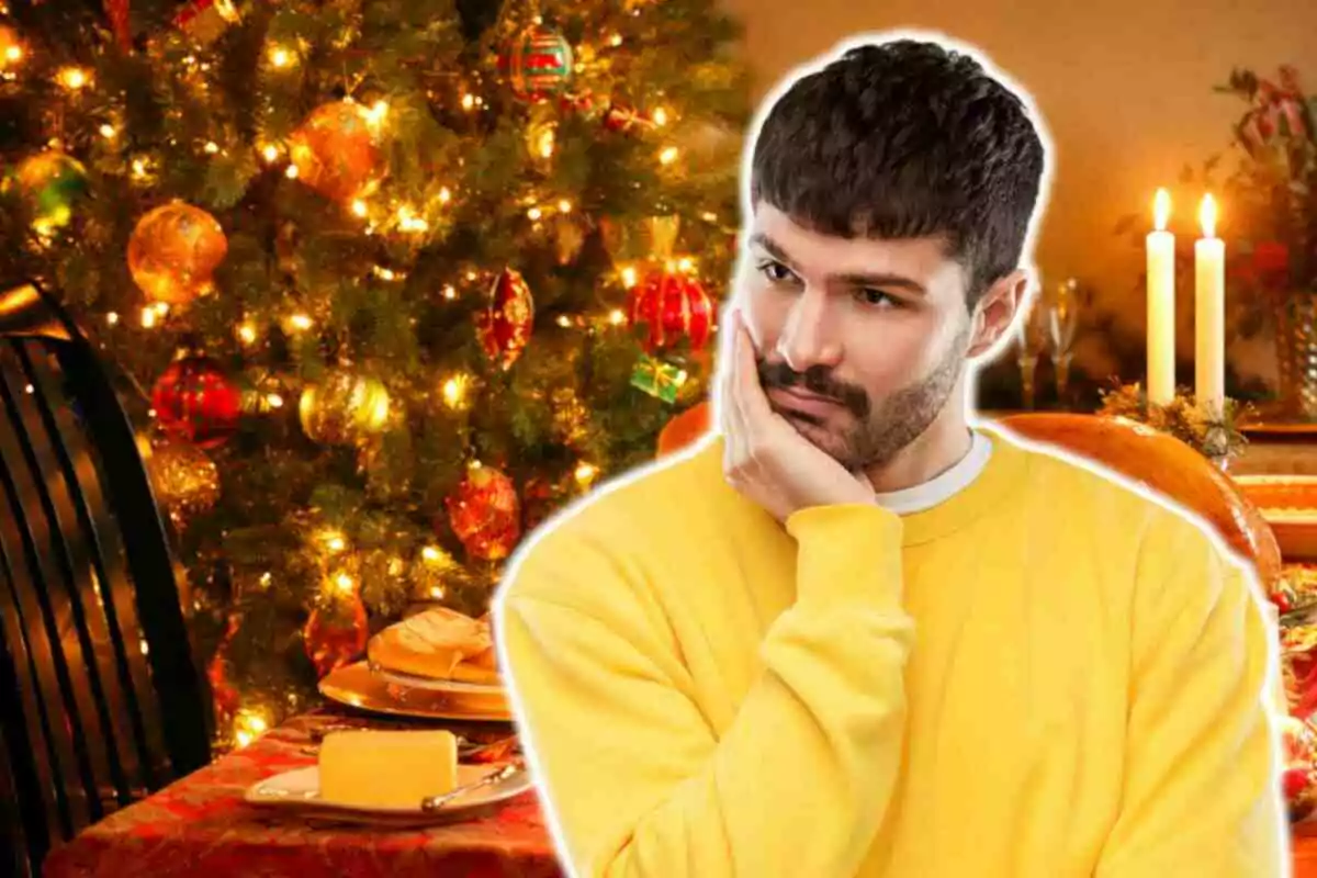 Hombre pensativo con su mano en la cara, vestido con un suéter amarillo, frente a un árbol de Navidad decorado y una mesa festiva iluminada por velas.