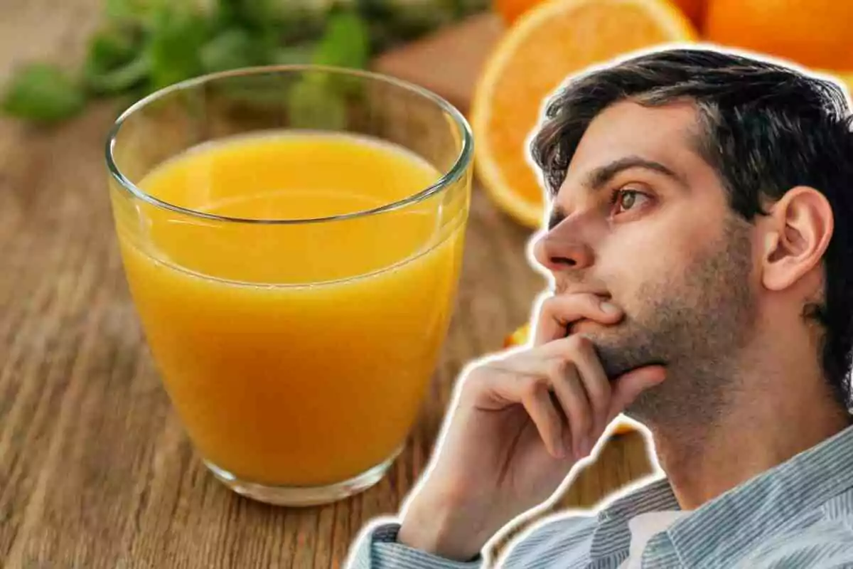 Un hombre pensativo junto a un vaso de jugo de naranja sobre una mesa de madera.