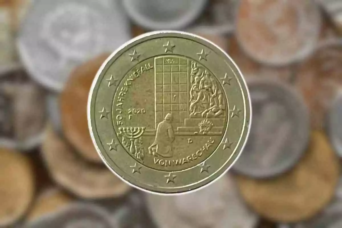 Moneda conmemorativa de dos euros con diseño que incluye una figura humana frente a un monumento y un candelabro, rodeada de estrellas sobre un fondo de otras monedas desenfocadas. Moneda conmemorativa de dos euros con diseño que incluye una figura humana frente a un monumento y un candelabro, rodeada de estrellas sobre un fondo de otras monedas desenfocadas.
