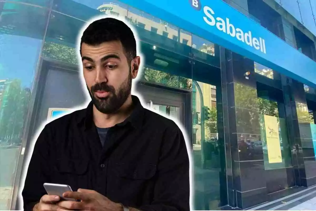 Un hombre con expresión sorprendida mira su teléfono móvil frente a una sucursal del Banco Sabadell.