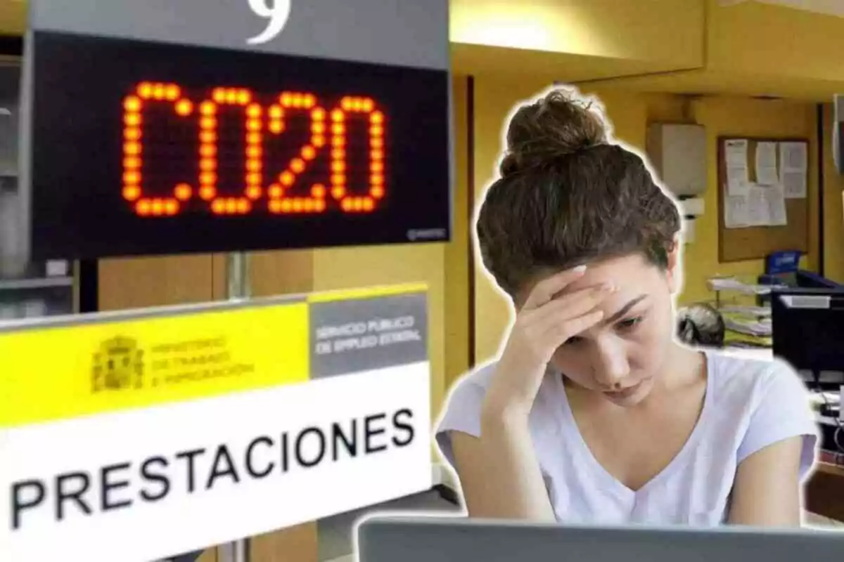 Una mujer con expresión preocupada en una oficina de prestaciones, con un letrero electrónico que muestra el número C020 y un cartel del Ministerio de Trabajo y Migraciones.