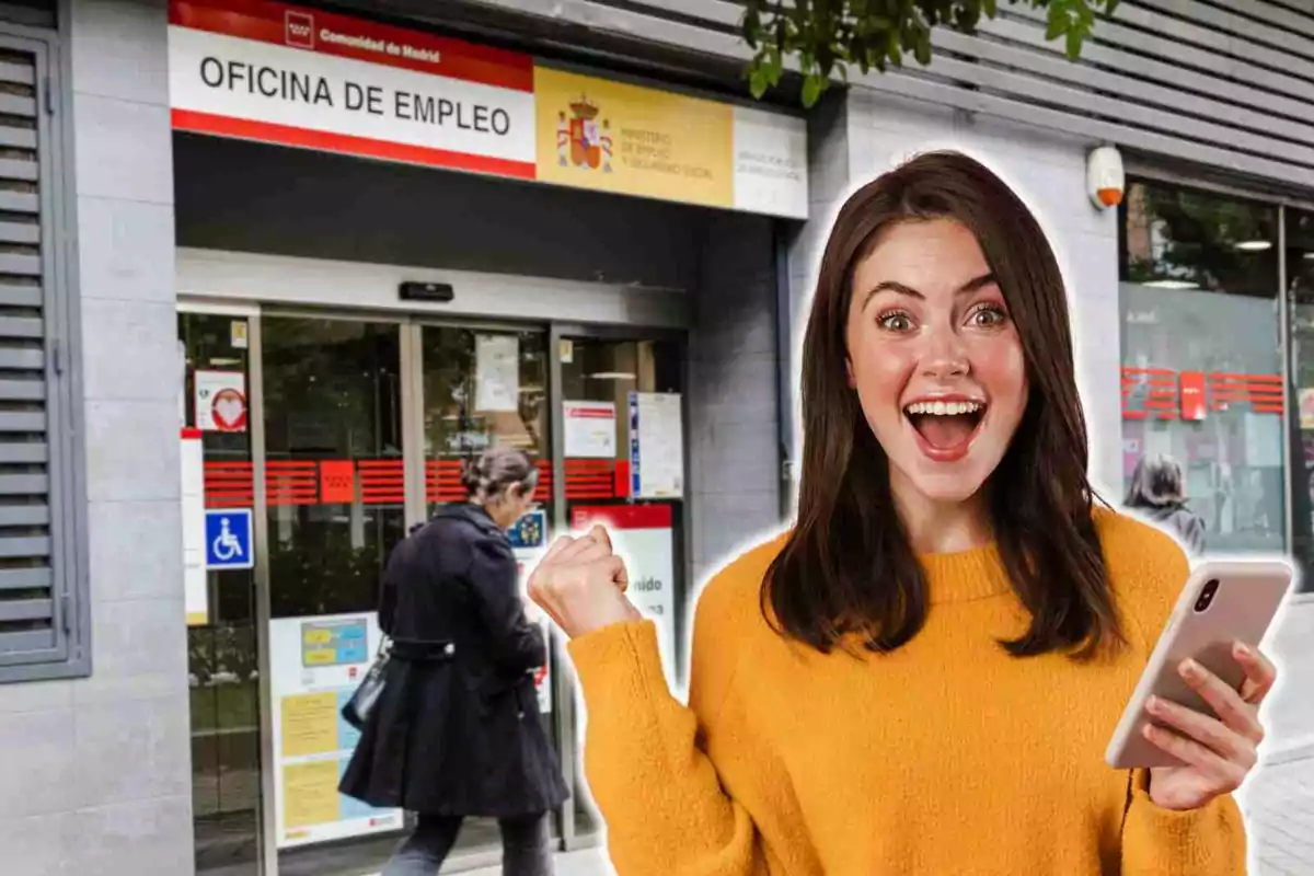 Una mujer sonriente con un teléfono móvil en la mano frente a una oficina de empleo.