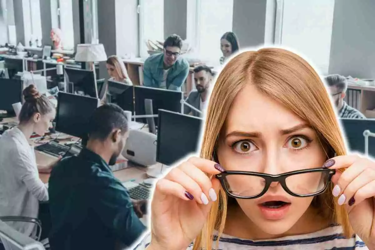Una mujer con expresión de sorpresa sostiene sus gafas frente a una oficina llena de personas trabajando en computadoras.