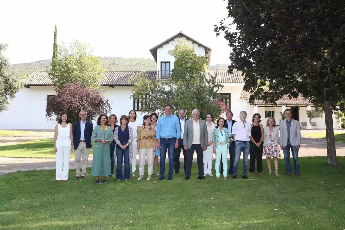 Un grupo de personas posando en un jardín frente a una casa blanca con árboles y césped verde Un grupo de personas posando en un jardín frente a una casa blanca con árboles y césped verde