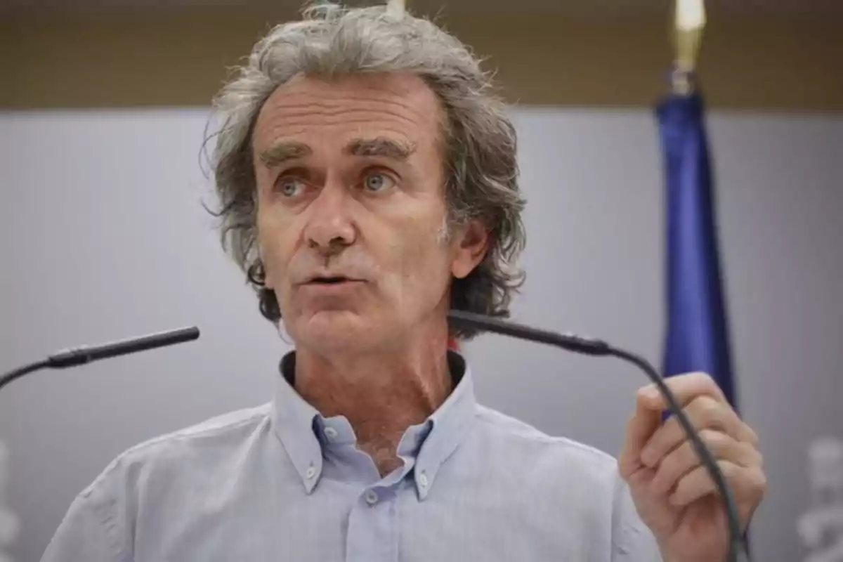 Un hombre de cabello canoso y camisa clara habla frente a un micrófono con una bandera en el fondo. Un hombre de cabello canoso y camisa clara habla frente a un micrófono con una bandera en el fondo.