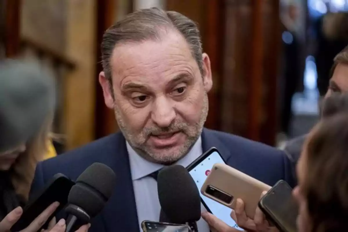 Un hombre en traje es entrevistado por varios periodistas que sostienen micrófonos y teléfonos móviles. Un hombre en traje es entrevistado por varios periodistas que sostienen micrófonos y teléfonos móviles.