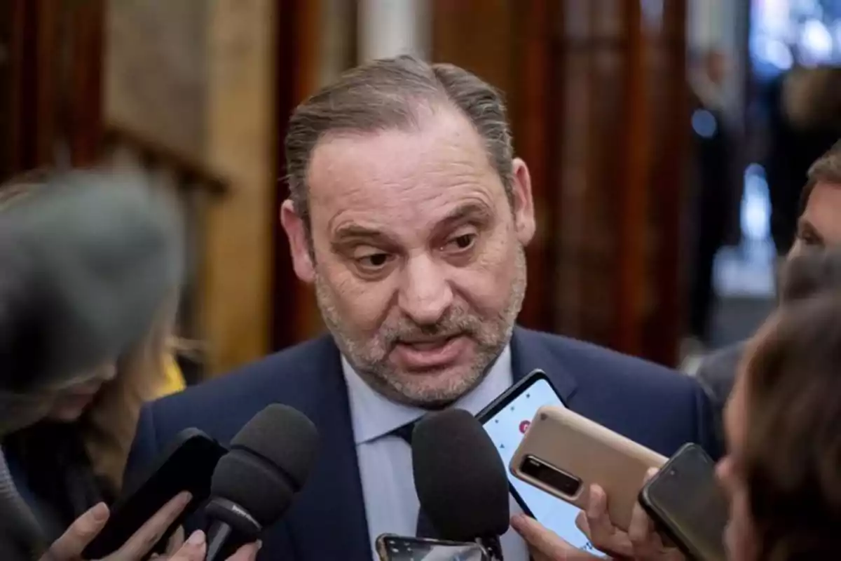 Un hombre con traje es entrevistado por varios periodistas que sostienen micrófonos y teléfonos móviles. Un hombre con traje es entrevistado por varios periodistas que sostienen micrófonos y teléfonos móviles.