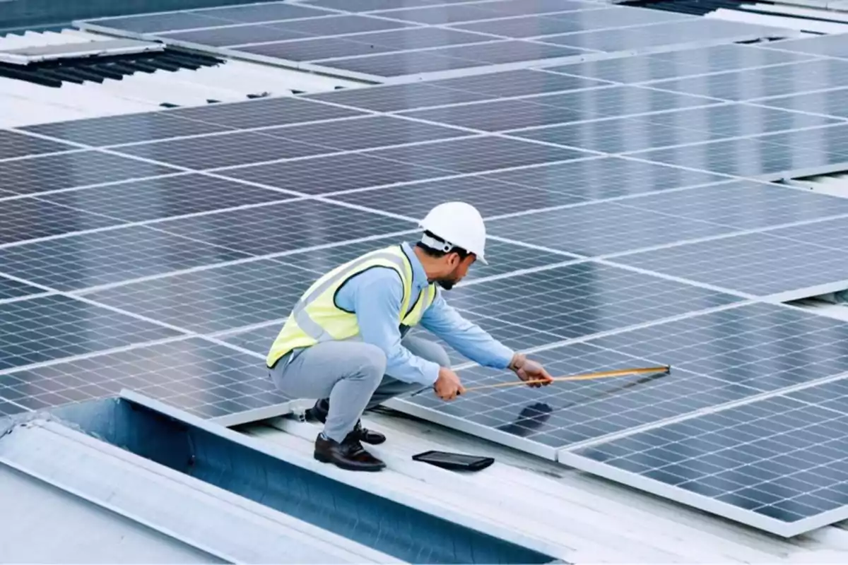 Trabajador con casco y chaleco midiendo paneles solares en un techo