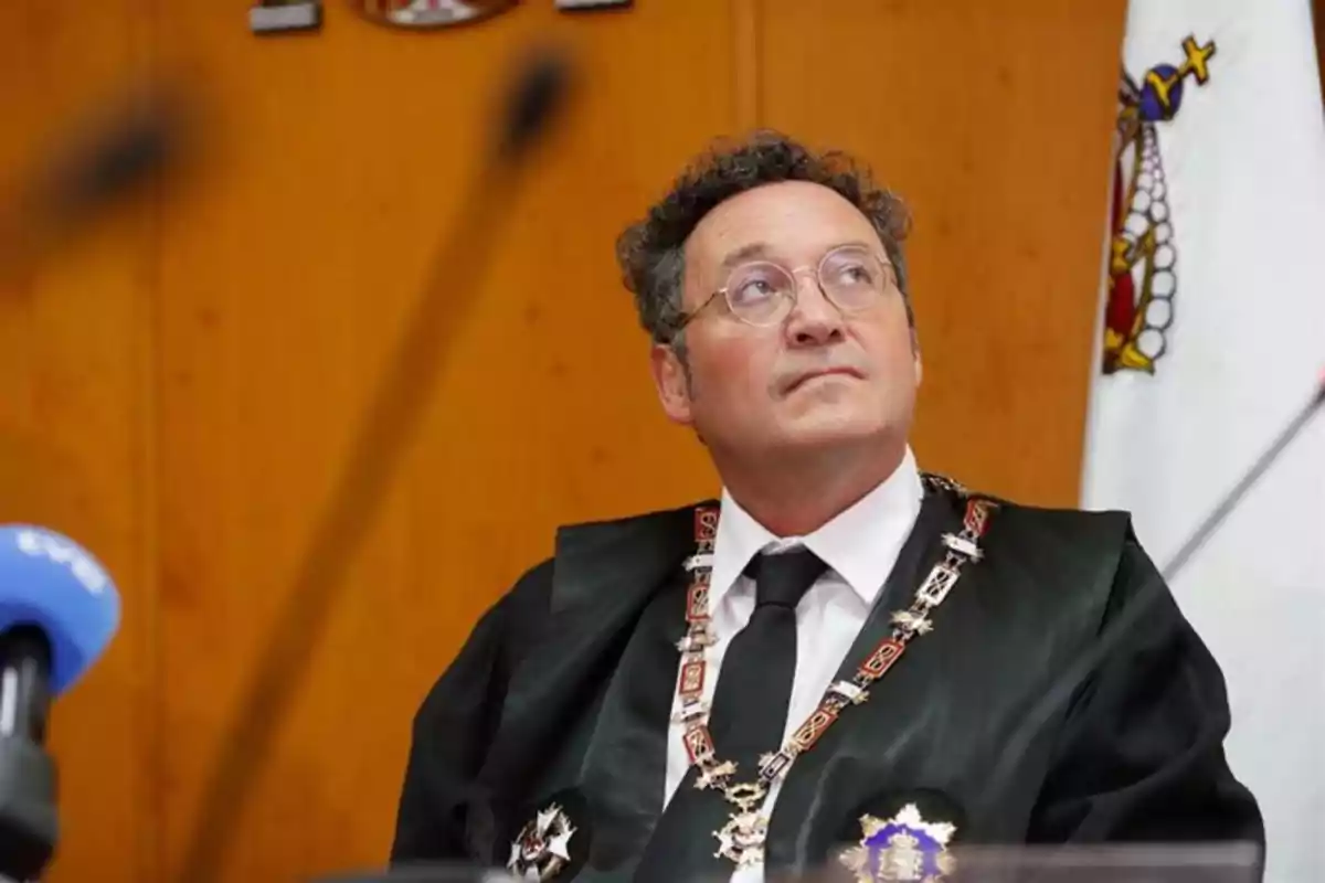 Un hombre con gafas y traje formal con medallas y una cadena ceremonial en un entorno oficial. Un hombre con gafas y traje formal con medallas y una cadena ceremonial en un entorno oficial.