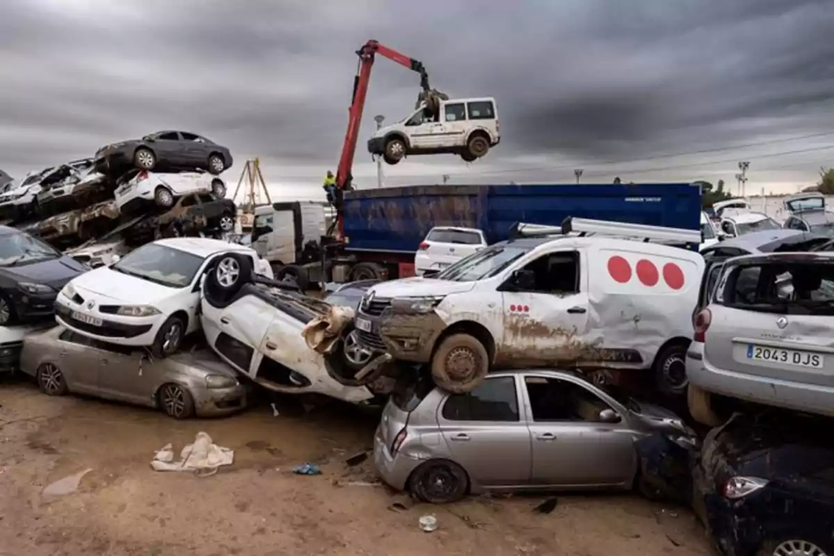 Un desguace de automóviles con varios coches apilados y un camión grúa levantando un vehículo bajo un cielo nublado.