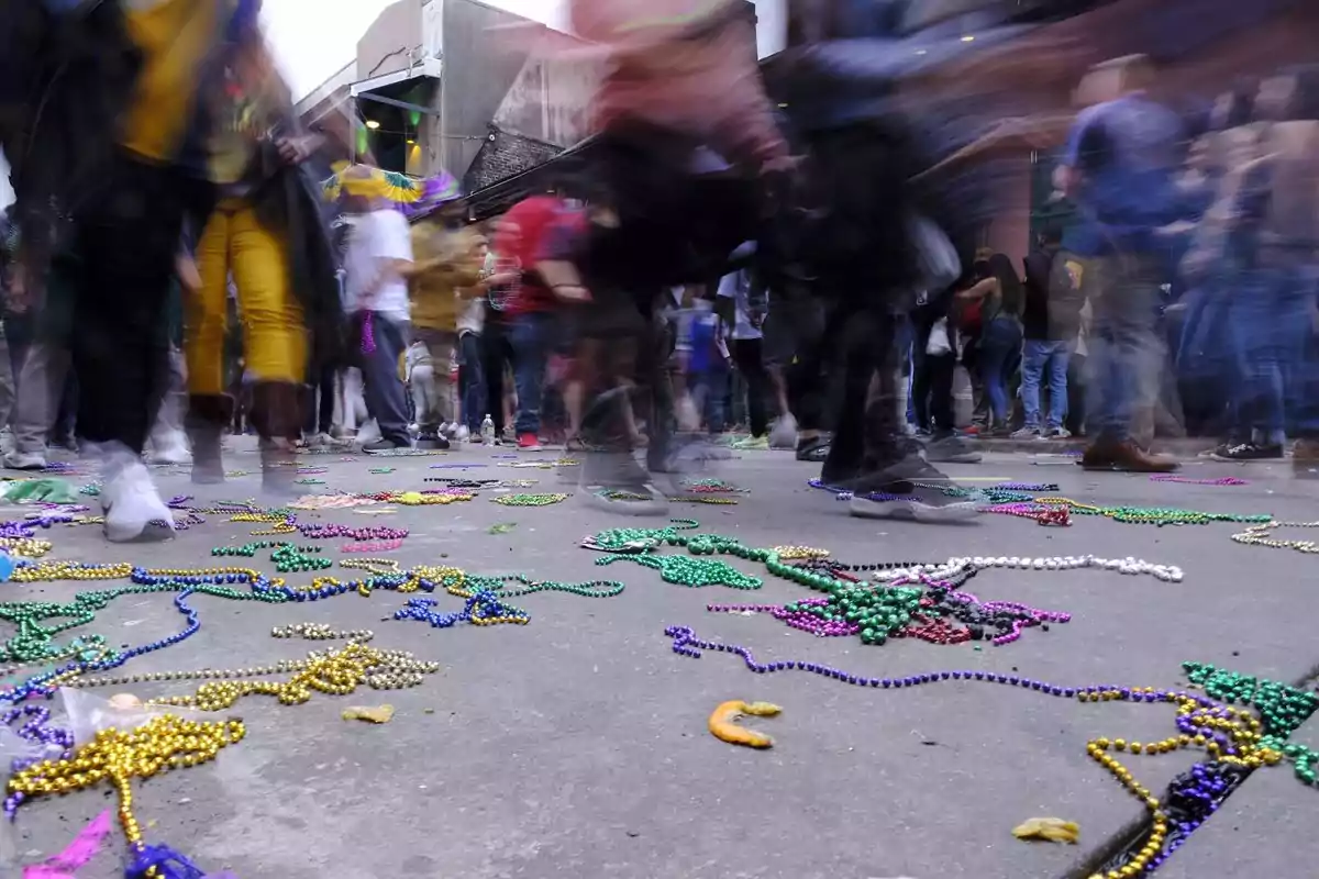 Personas caminando en una calle llena de collares de cuentas de colores esparcidos por el suelo durante un evento festivo.