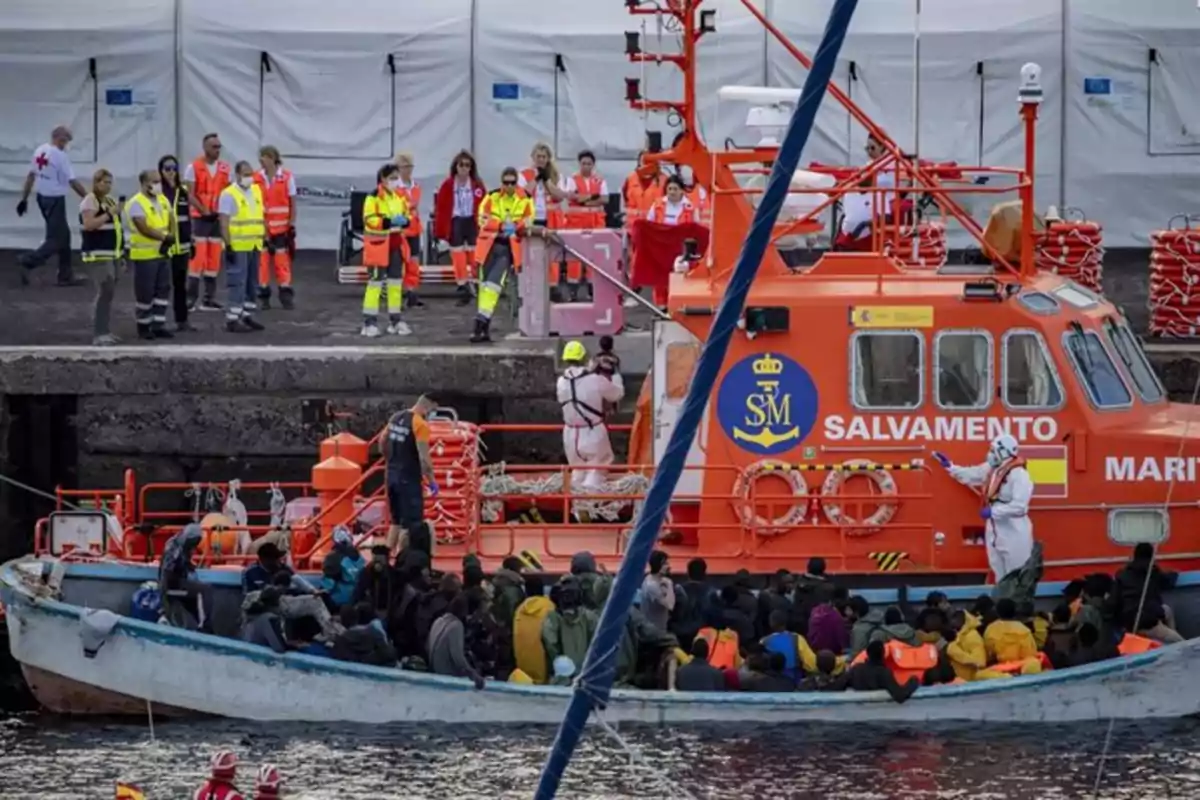 Un grupo de personas es rescatado por un barco de Salvamento Marítimo mientras personal de emergencia espera en el muelle. Un grupo de personas es rescatado por un barco de Salvamento Marítimo mientras personal de emergencia espera en el muelle.