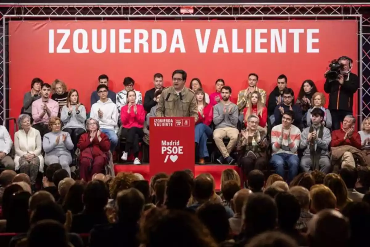 A group of people is gathered at a political event with a speaker at a red podium that says "Madrid PSOE" and a background that says "Brave Left."