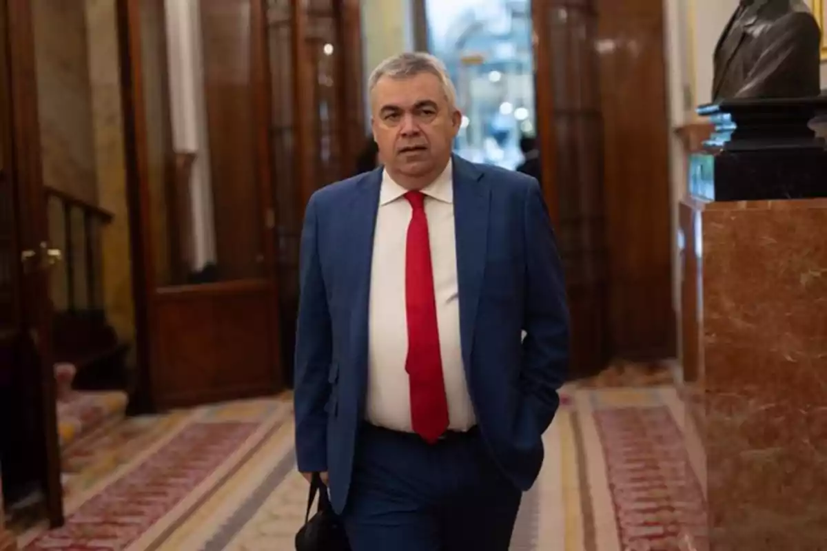 Hombre de cabello canoso con traje azul y corbata roja caminando por un pasillo elegante con alfombra y paredes de madera Hombre de cabello canoso con traje azul y corbata roja caminando por un pasillo elegante con alfombra y paredes de madera