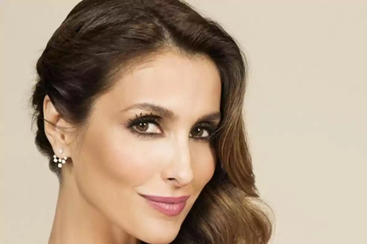 Una mujer con cabello castaño y maquillaje elegante sonríe ligeramente mirando hacia la cámara. Una mujer con cabello castaño y maquillaje elegante sonríe ligeramente mirando hacia la cámara.