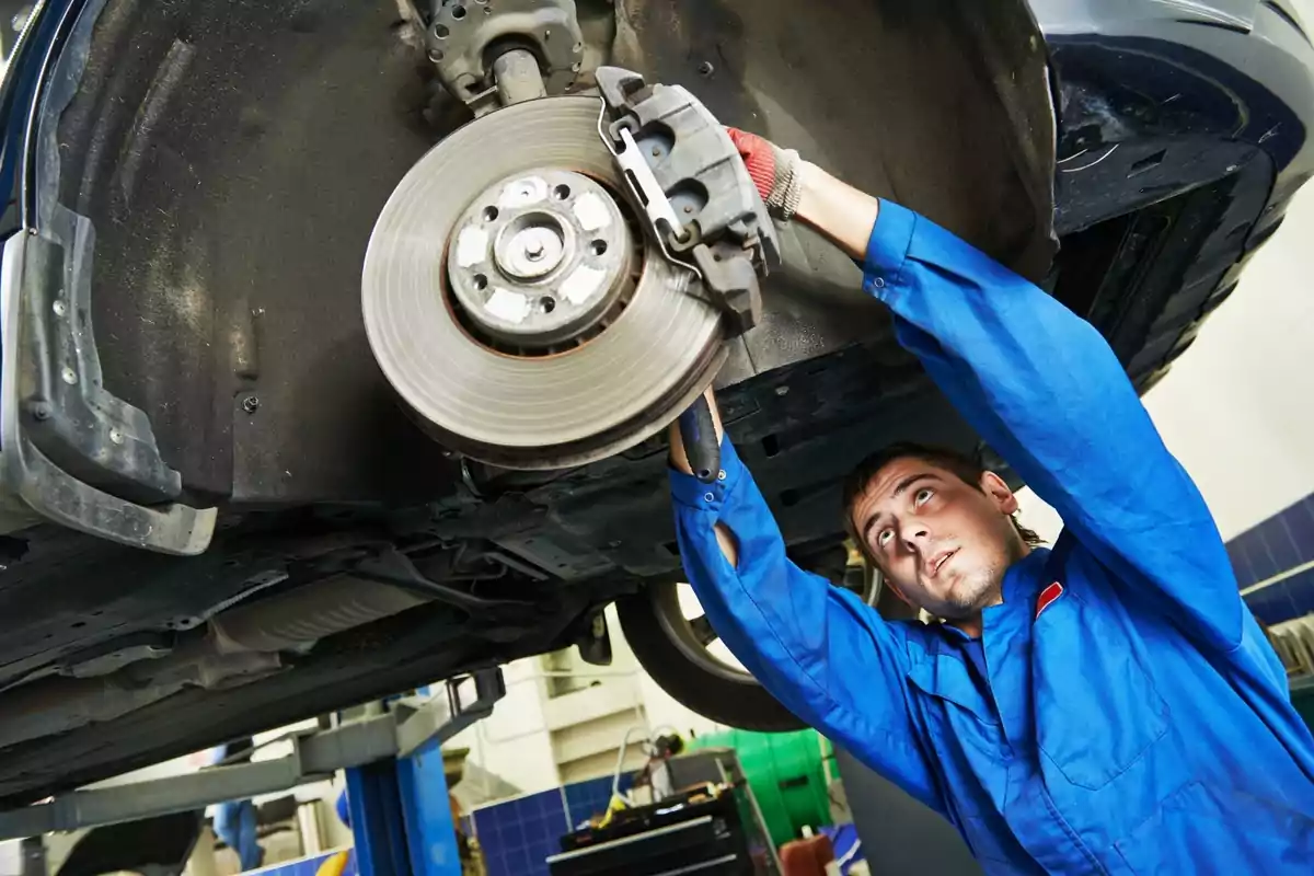 Mecánico trabajando en el sistema de frenos de un automóvil elevado en un taller.