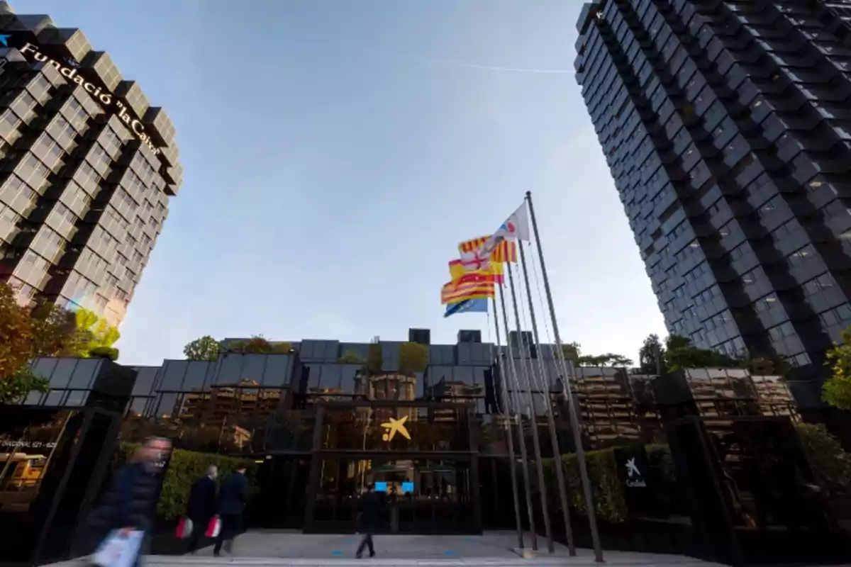 Edificio moderno con fachada de vidrio y varias banderas ondeando al frente.