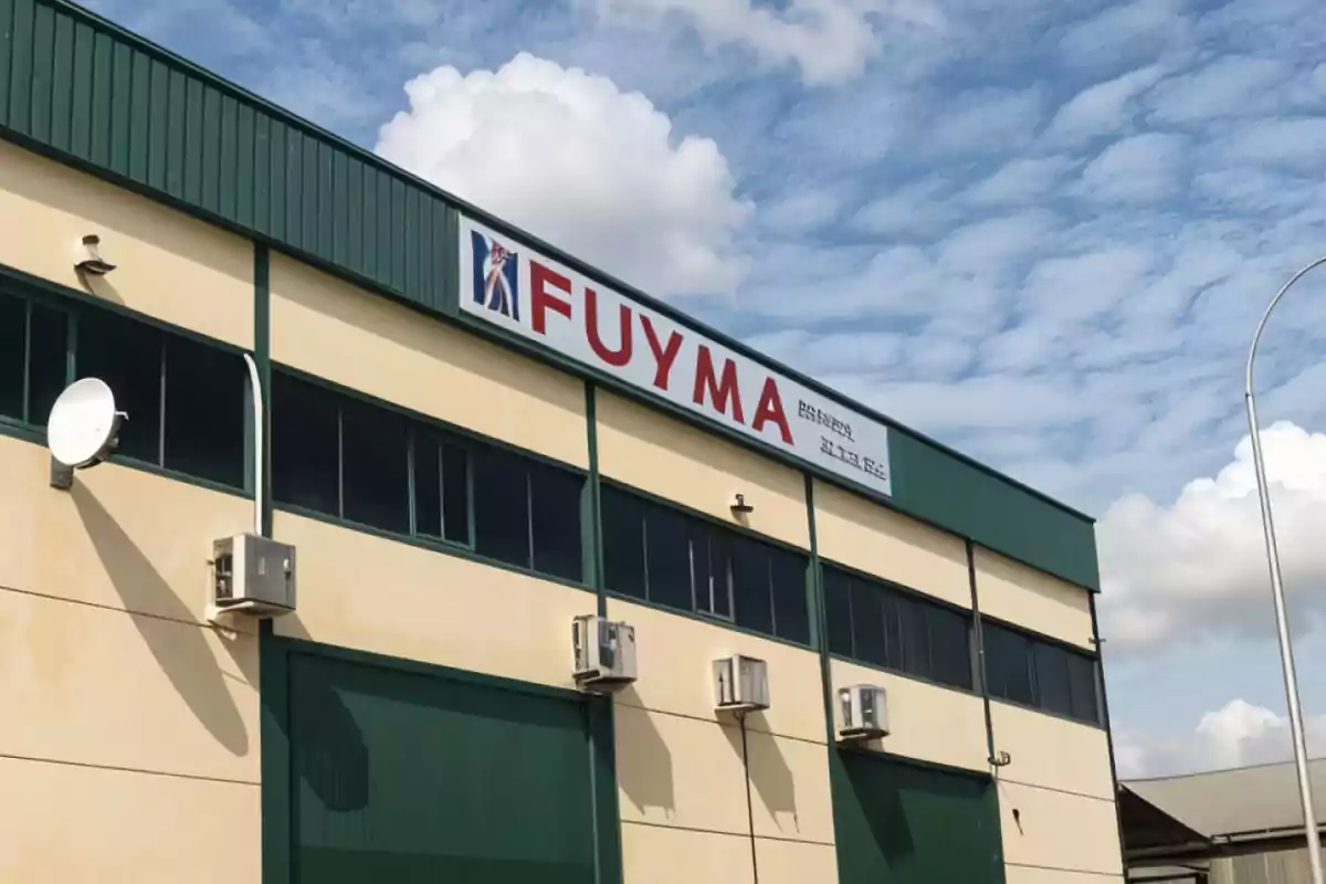 Edificio industrial con un letrero que dice FUYMA bajo un cielo parcialmente nublado.