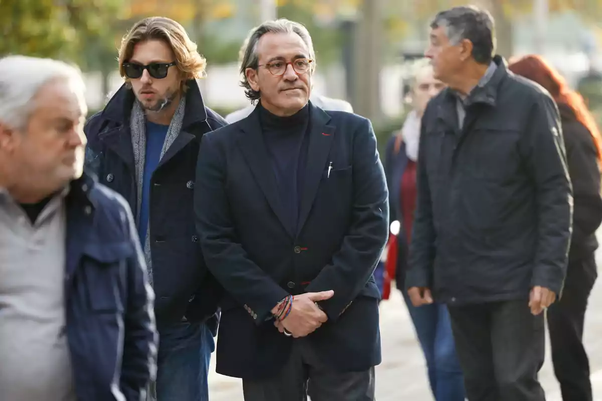 Un grupo de personas caminando al aire libre, algunas de ellas con abrigos y gafas de sol.