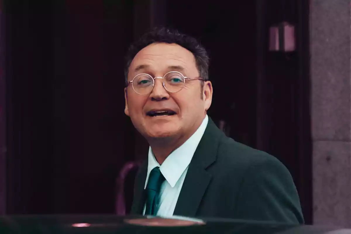 Hombre de mediana edad con gafas y traje verde oscuro mirando hacia la cámara con expresión amigable