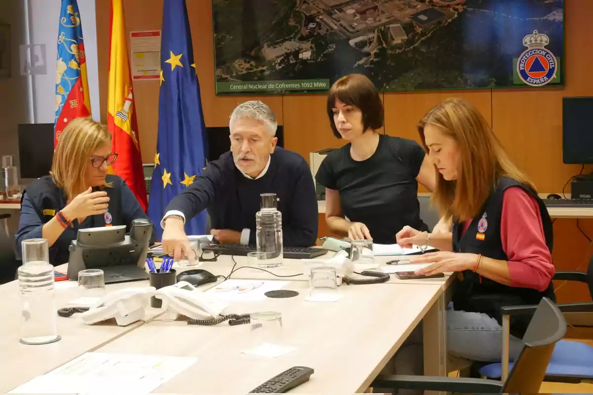 Un grupo de personas se encuentra reunido en una sala de conferencias, con banderas de fondo y documentos sobre la mesa, mientras discuten y revisan información.