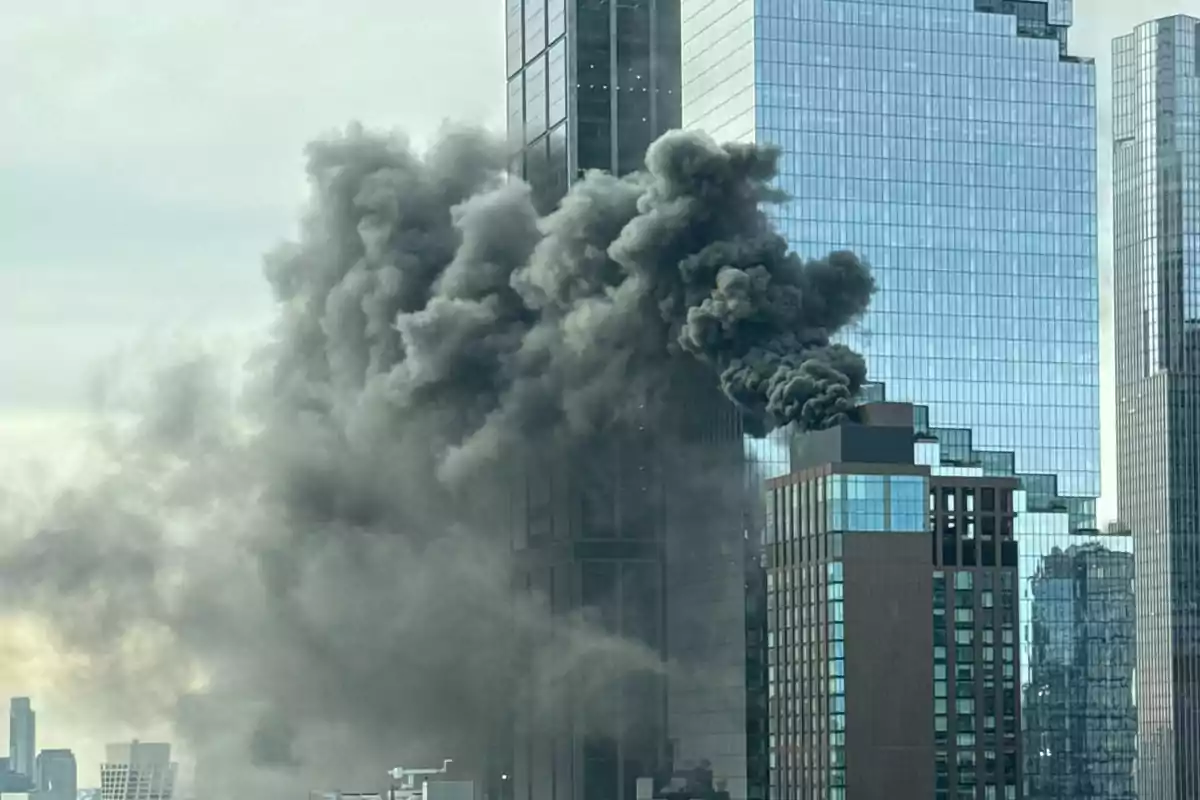 Un edificio alto con humo negro saliendo de su parte superior en un entorno urbano.